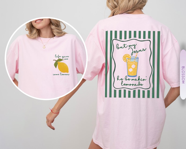 May include: A light pink t-shirt with a lemon graphic on the front and a lemonade graphic on the back. The front of the shirt says "life gave me some lemons." The back says "but my Jesus he be makin' lemonade."