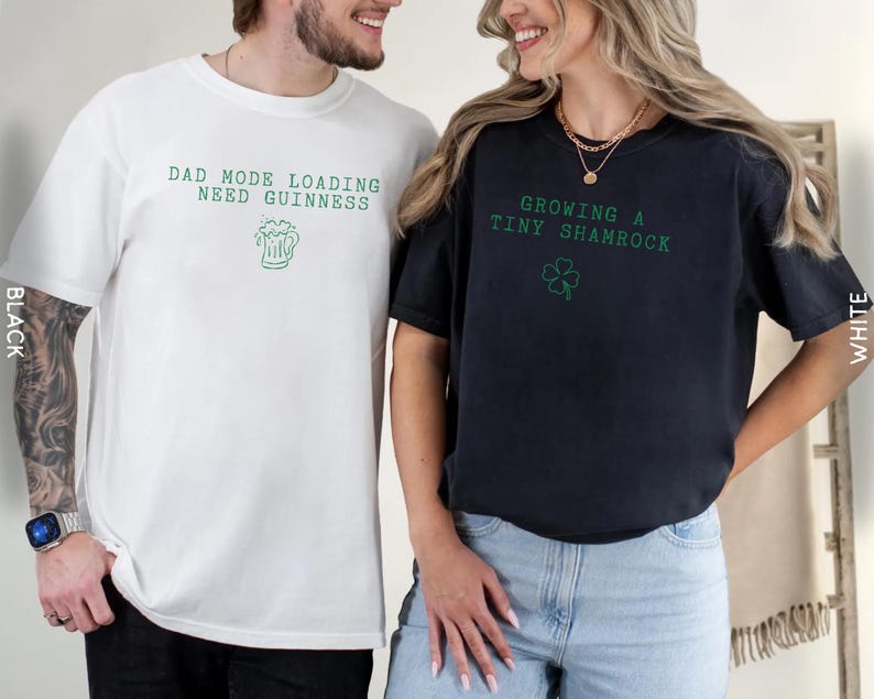 K&ouml;nnte beinhalten: Zwei T-Shirts, eines wei&szlig; und eines schwarz, mit gr&uuml;nem Text und Grafiken. Das wei&szlig;e Shirt sagt "DAD MODE LOADING NEED GUINNESS" mit einer Bierkrug-Grafik. Das schwarze Shirt sagt "GROWING A TINY SHAMROCK" mit einem Kleeblatt.