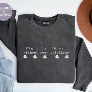 May include: Dark gray crewneck sweatshirt with the text "Fight for those without your privilege" and daisy graphics. The sweatshirt is part of a clothing collection.