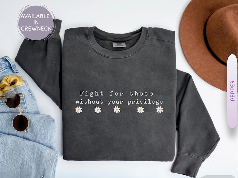May include: Dark gray crewneck sweatshirt with the text "Fight for those without your privilege" and daisy graphics. The sweatshirt is part of a clothing collection.