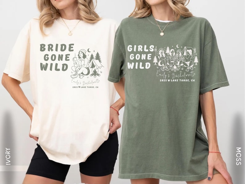 Puede incluir: Dos camisetas holgadas, una marfil y otra verde musgo, con texto gr&aacute;fico e ilustraciones. La camiseta marfil dice "BRIDE GONE WILD" con una escena de acampada. La camiseta verde dice "GIRLS GONE WILD" con una escena de acampada en grupo. Ambas camisetas incluyen "Emily's Bachelorette" y la ubicaci&oacute;n.