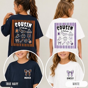 Peut inclure: Deux t-shirts à manches courtes, bleu marine et blanc. Le dos présente un cadre à rayures verticales avec le texte "COUSIN crew" et des icônes d'Halloween. La poitrine gauche affiche un nœud avec un prénom, "MARIA" ou "EMILY".