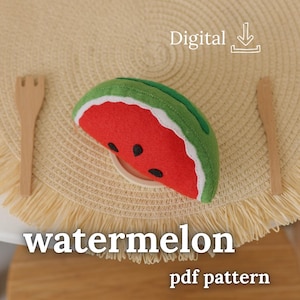 Può includere: Una fetta di anguria in feltro con interno rosso, semi neri, buccia bianca e bordo esterno verde. Il testo Digital e un'icona di download appaiono sopra, con il testo watermelon pdf pattern stampato sotto la fetta di frutta in feltro.