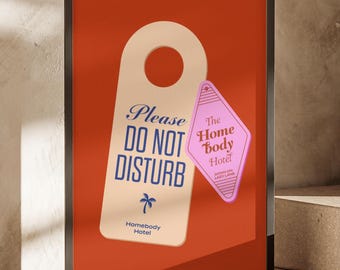 May include: A framed poster with a red background features a cream-colored door hanger with the words "Please DO NOT DISTURB" in blue script. A pink diamond-shaped hotel key tag reads "The Home Body Hotel" in white. The poster is in a black frame.