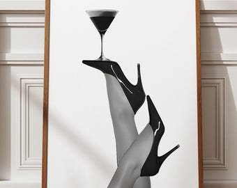 May include: Black and white art print featuring a martini glass balanced on a high-heeled shoe. The image showcases a pair of legs in black heels, with one leg crossed over the other. The martini glass is filled with a dark liquid.