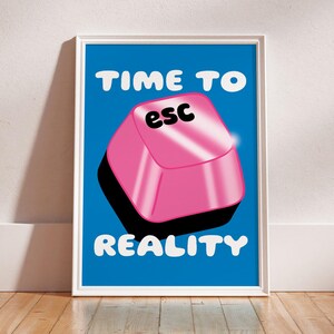 May include: A framed art print with a blue background and white text that reads "TIME TO ESC REALITY." A large pink "esc" key graphic is centered. The print is in a white frame and set against a white wall and wooden floor.