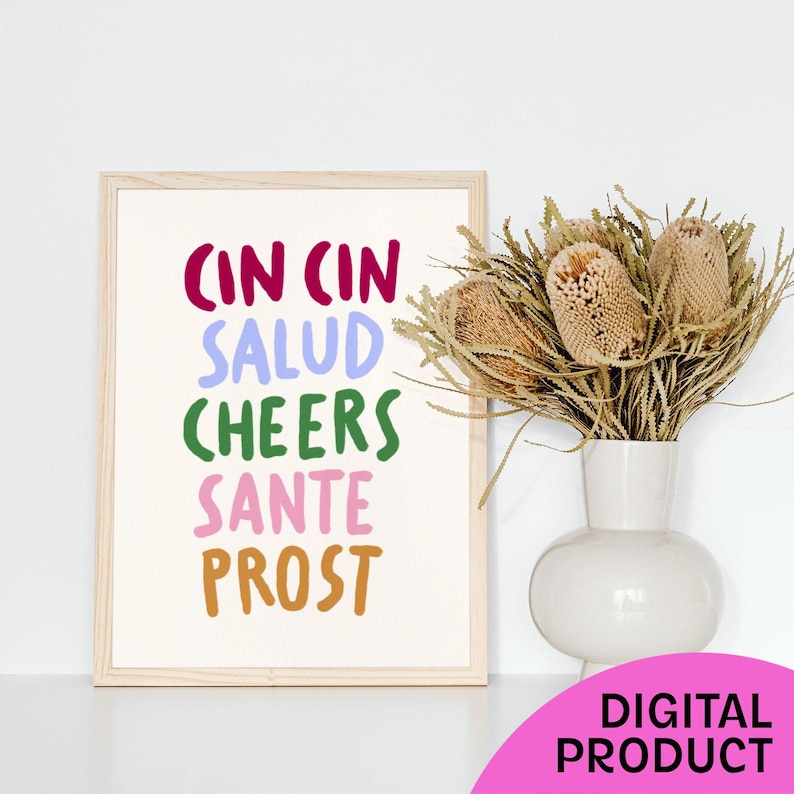 May include: A framed print with the words "CIN CIN SALUD CHEERS SANTE PROST" in various colours. A white vase with dried flowers sits to the right of the print. A pink circle with the words "DIGITAL PRODUCT" is in the lower right corner.