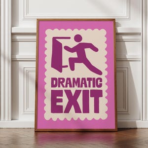 May include: A framed print with a pink background and a cream-colored, postage stamp-shaped design. The design features a purple stick figure running through a door, with the words "DRAMATIC EXIT" in purple block letters.