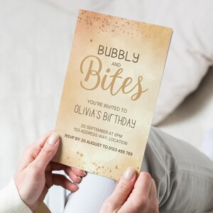 Könnte beinhalten: Eine goldene und weiße Einladungskarte mit Aquarellhintergrund und goldenem Glitzer. Der Text lautet "Bubbly and Bites You're invited to Olivia's Birthday 20 September at 6pm 123 Address Way, Location RSVP by 20 August to 0123 456 789".