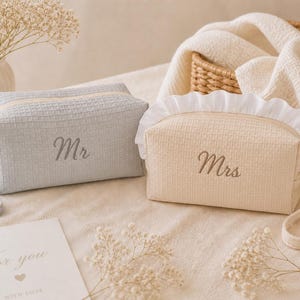 May include: Two matching cosmetic bags, one light gray and one cream, with waffle texture. The gray bag has "Mr" embroidered on it, and the cream bag has "Mrs" embroidered. Both have a zipper closure and a handle.