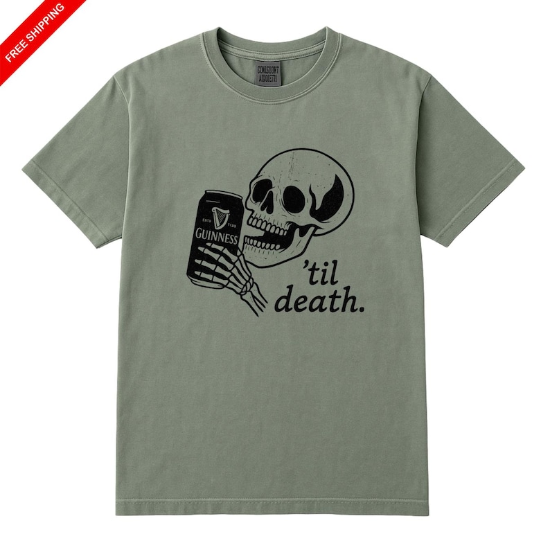 May include: Sage green t-shirt featuring a black graphic of a skull holding a Guinness can, with the phrase "'til death." printed below. The shirt has a crew neck and short sleeves.
