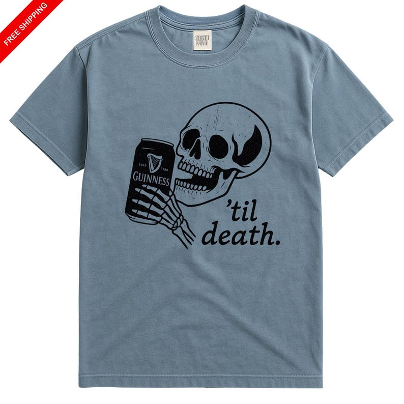 May include: Dusty blue t-shirt featuring a black graphic of a skull holding a Guinness can with a skeleton hand. The text "'til death" is below the skull. The shirt has a crew neck and short sleeves.