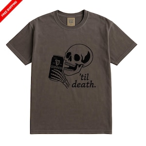 May include: A brown t-shirt features a black graphic of a skull holding a Guinness can with the text "'til death." The shirt has a crew neck and short sleeves. The brand name "Capery Crows" is printed on the upper back.