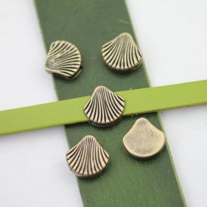 Puede incluir: Cinco abalorios de metal en forma de concha de color dorado antiguo sobre un fondo de cuero verde.