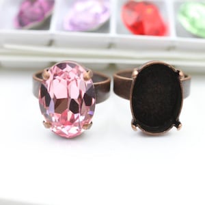 May include: Two antique bronze rings. One ring features a large, faceted, oval-cut pink gemstone. The other ring has an empty oval setting. The rings are set against a white background, with a glimpse of other gemstones in the background.