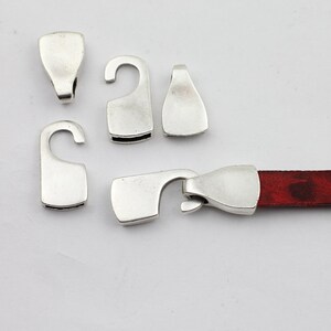 May include: Silver-toned metal clasps for leather straps. The clasps have a hook and loop design. One clasp is attached to a red leather strap.