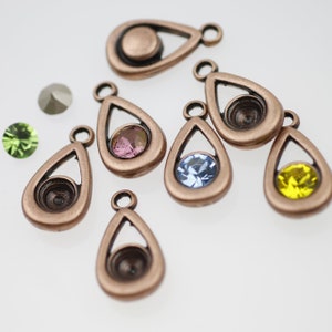 Könnte beinhalten: Sortiment aus acht kupferfarbenen Anhänger-Anhängern in Tropfenform mit einer klaren Zargenfassung. Jeder Anhänger ist mit einem andersfarbigen Edelstein besetzt: grün, rosa, blau und gelb.