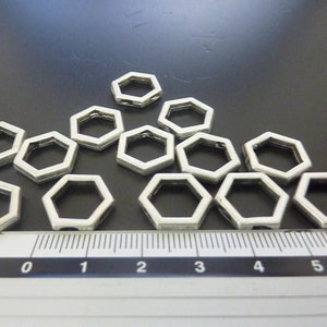 May include: A group of silver-toned metal hexagonal jump rings, approximately 1 inch in diameter, arranged in a triangular pattern on a black surface. A ruler is visible in the bottom of the image.