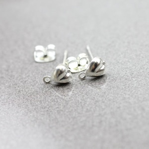 May include: Two silver heart-shaped earring findings with a loop on the side. The findings are on a grey surface.