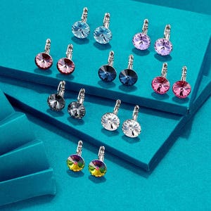 Puede incluir: Surtido de gemelos con gemas de colores, incluyendo azul, rojo, morado y transparente. Los gemelos están dispuestos en pares sobre una superficie azul.