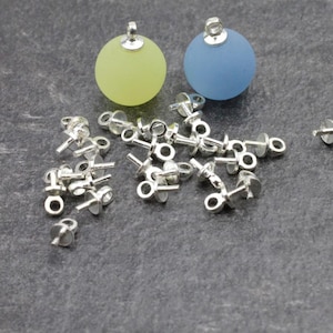 May include: A collection of silver-colored earring posts and two round, frosted glass beads. One bead is yellow-green, the other is blue. The earring posts have a small, flat disc and a loop for attaching the earring.
