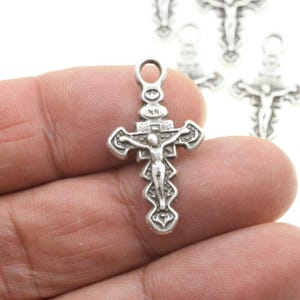 May include: Silver-toned metal crucifix charm with a detailed design of a figure on the cross. The charm has a loop at the top for attaching to a necklace or bracelet.
