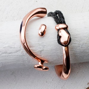 May include: Two rose gold bracelets, one with a heart charm and the other with a simple design. Both bracelets are on a white surface.