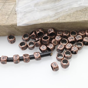 May include: A close-up of a pile of copper-coloured metal beads with a black leather cord threaded through some of the beads. The beads have a textured surface and appear to have small markings on them.