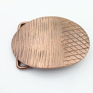 Può includere: Una fibbia ovale per cintura in tono rame con un design testurizzato. Una metà della fibbia presenta un motivo a linee verticali, mentre l'altra metà presenta un motivo a rombi.