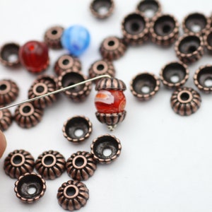 May include: A close-up of a red and white glass bead with copper-colored metal bead caps. The bead is threaded on a thin wire.