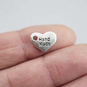 May include: Silver heart-shaped charm with a hole at the top and the words "Hand Made" engraved on the front.