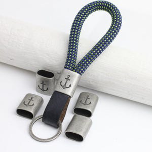 May include: A silver key chain with a blue and green rope loop and a silver anchor charm. The key chain has five additional silver charms with anchor designs.
