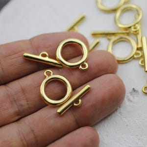 Op de afbeelding: Gouden metalen schuifgespen met een ronde ring en een rechte stang. De gespen zijn perfect voor het maken van sieraden, tassen en andere knutselprojecten.