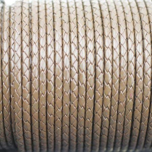 May include: Close-up of a reel of brown braided leather cord. The cord is woven in a diamond pattern.