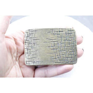 May include: A brass belt buckle with a textured, crosshatch pattern.
