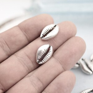 May include: Two silver cowrie shell charms. The shells are smooth and have a slightly textured surface.