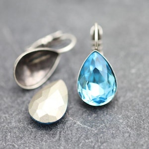 Puede incluir: Un par de pendientes de plata en forma de lágrima con un cristal azul claro. Los pendientes tienen un cierre de clip.