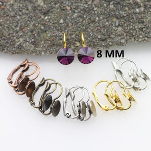 Peut inclure: Un ensemble de montures de boucles d'oreilles de 8 mm en or, argent et bronze. Les montures sont conçues pour recevoir une pierre ronde en cabochon. L'image montre également une paire de boucles d'oreilles avec des pierres violettes.