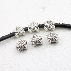 May include: Six silver charm beads in the shape of a carriage. The beads are strung on a black leather cord.