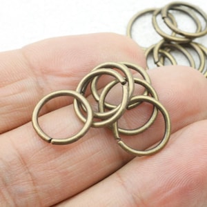 May include: A close-up of a pile of antique gold-toned metal jump rings. The rings are all the same size and are arranged in a random pattern.