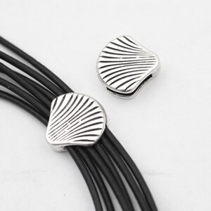 Puede incluir: Dos cierres de metal en forma de concha de color plateado para un collar o pulsera de múltiples hebras. Los cierres están diseñados para sujetar múltiples hebras de cordón o cuero.