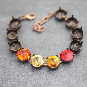 May include: A copper-toned bracelet with a chain and a row of round settings. The settings are filled with red, orange, and yellow gemstones.