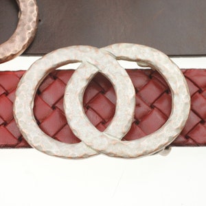 May include: A silver-toned, double-loop belt buckle with a hammered texture. The buckle is on a red woven leather belt.