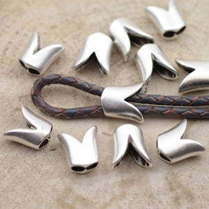 May include: Silver metal cord ends with a V-shaped design. The cord ends are shown on a brown leather cord.