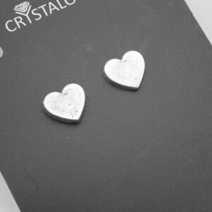 May include: A pair of silver heart-shaped stud earrings. The earrings are small and have a slightly textured surface.
