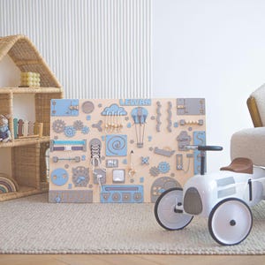 A large blue activity board for toddler with mazes, a sorter, doors and other play elements.