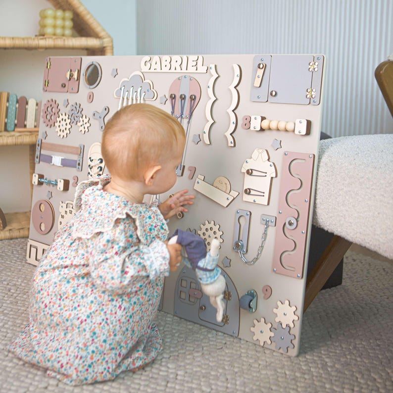 A child playing with a pastel Montessori sensory board standing on a beige carpet.