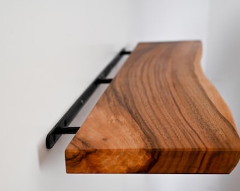 May include: A wooden shelf with a live edge and a black metal bracket. The shelf is made of natural wood with a rich brown color and a unique grain pattern.
