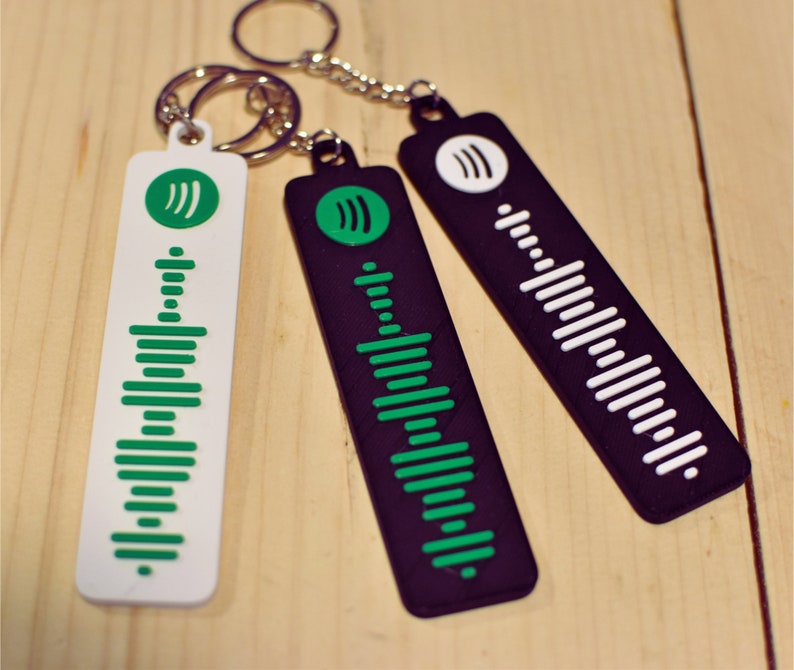 May include: Three keychains featuring a sound wave design. One keychain is white with green sound waves, one is black with green sound waves, and one is black with white sound waves.