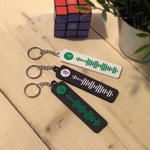May include: Three black keychains with green and white Spotify logos and barcodes. The keychains are on a wooden surface.